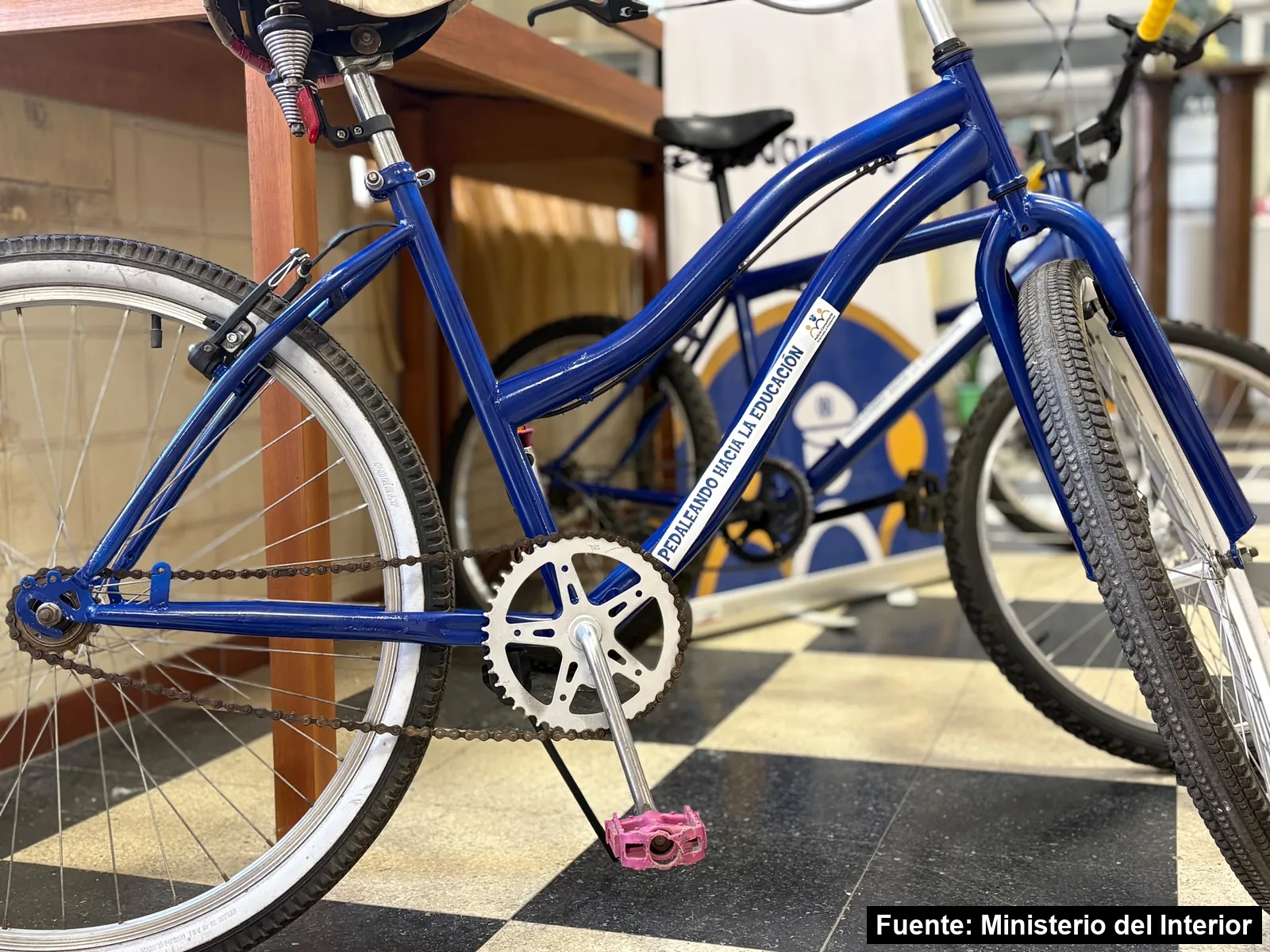 Mayo Amarillo en Paso de los Toros 2 Bicicleta azul restaurada con la etiqueta Pedaleando hacia la educación, sobre un piso de baldosas en damero