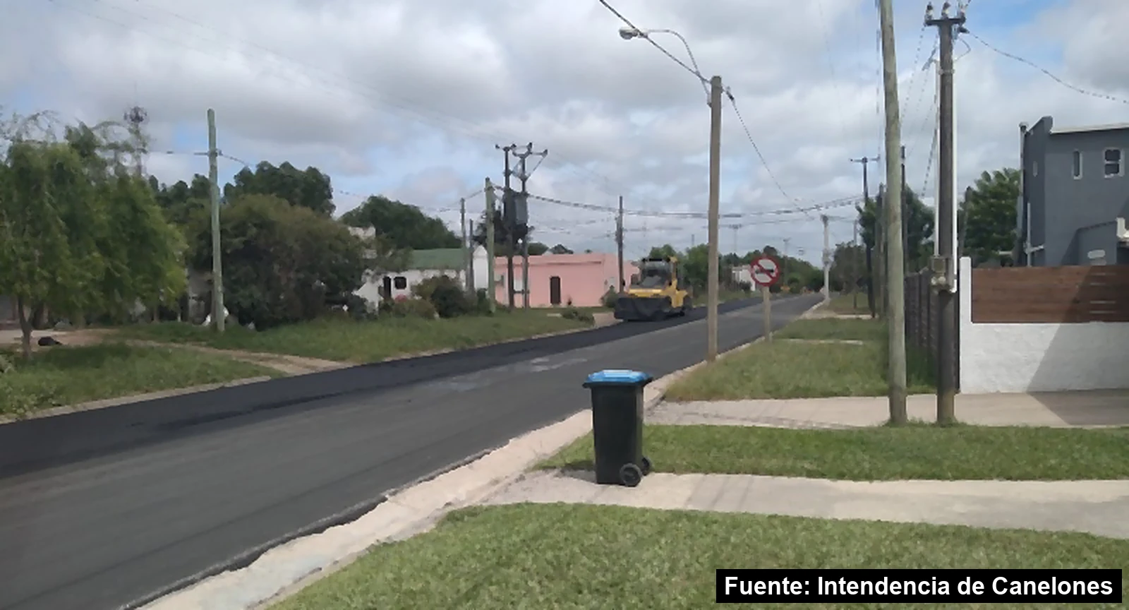 Calle recién pavimentada en San Bautista, con una aplanadora al fondo y una señal de tránsito en la vereda