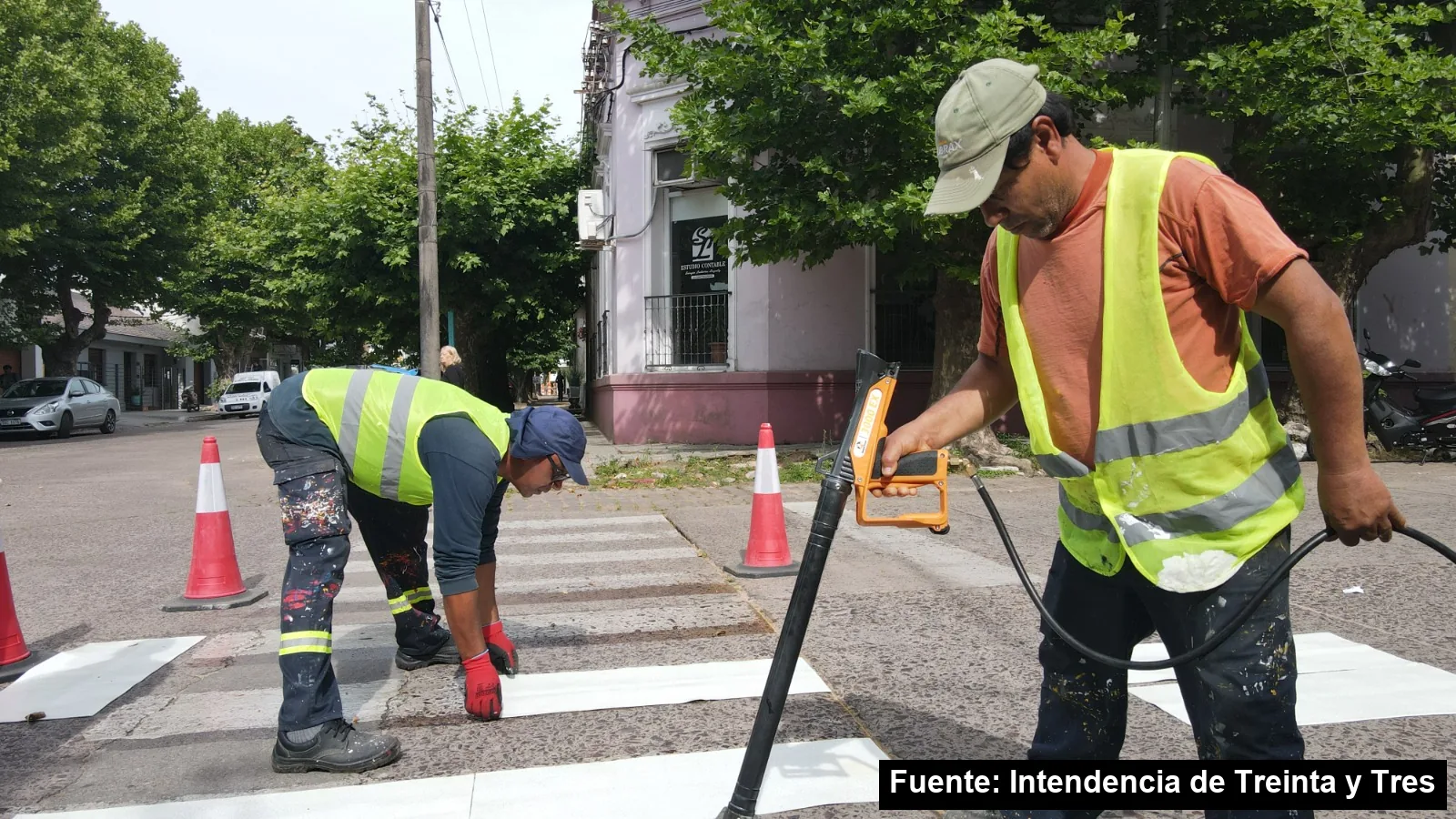 Dos operarios de la Dirección de Tránsito, con chalecos reflectivos, colocan las franjas blancas de un cruce peatonal adhesivo entre conos