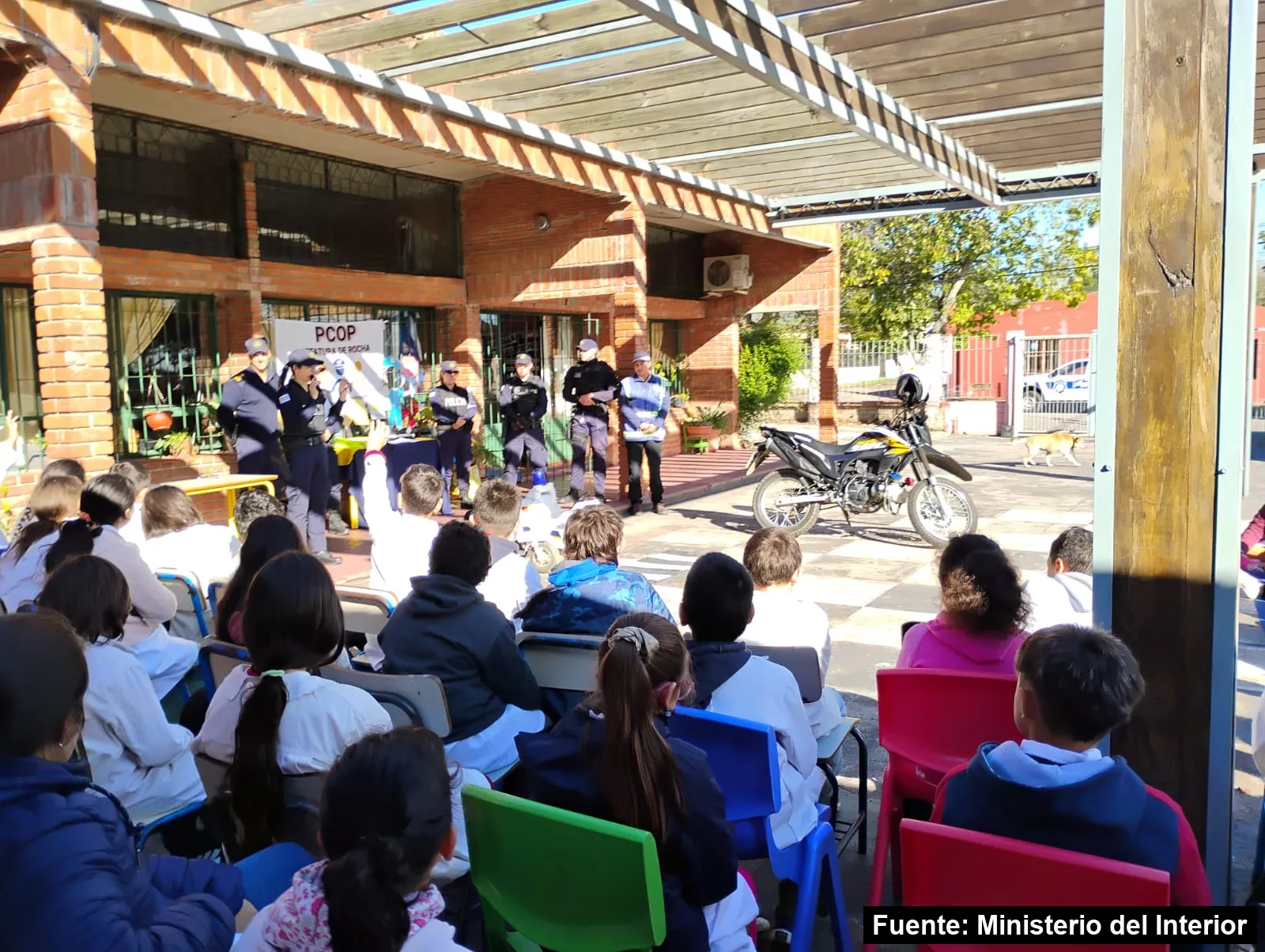 Mayo Amarillo en Lascano 2 Escolares sentados de espaldas escuchan a policías y a un inspector de tránsito en el patio de una escuela de Lascano, con una moto policial al costado