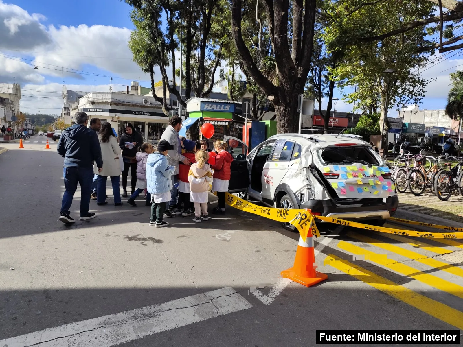 Escolares junto a un auto chocado cubierto de mensajes adhesivos en la feria de Mayo Amarillo de Canelones