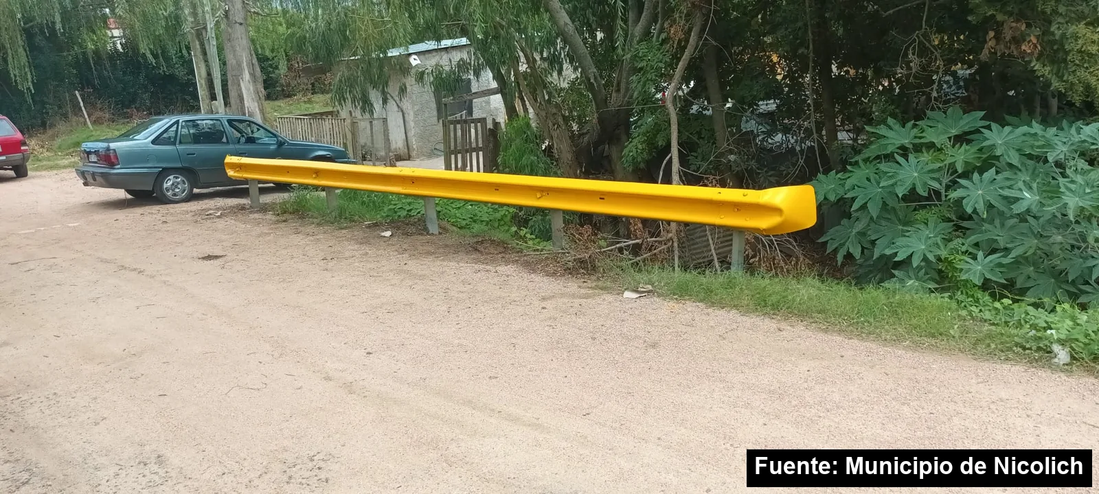 Guardarrail recién pintado de amarillo al costado de una calle de tierra en un barrio de Nicolich