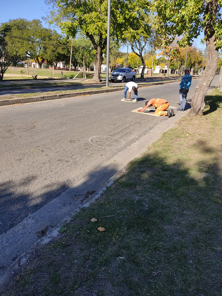 Mayo Amarillo en Colonia Valdense 2 Dos hombres marcan con plantillas los círculos sobre el asfalto de una avenida de Colonia Valdense mientras un tercero mira desde el cantero
