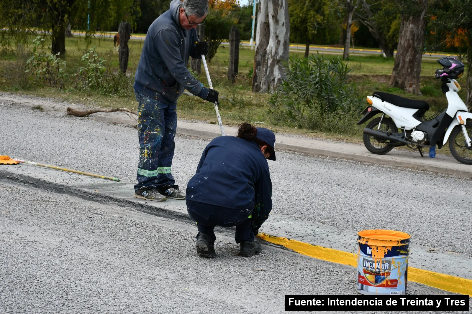 Dos trabajadores de la Intendencia pintan de amarillo el cordón del cantero central del bulevar Ariel Pinho
