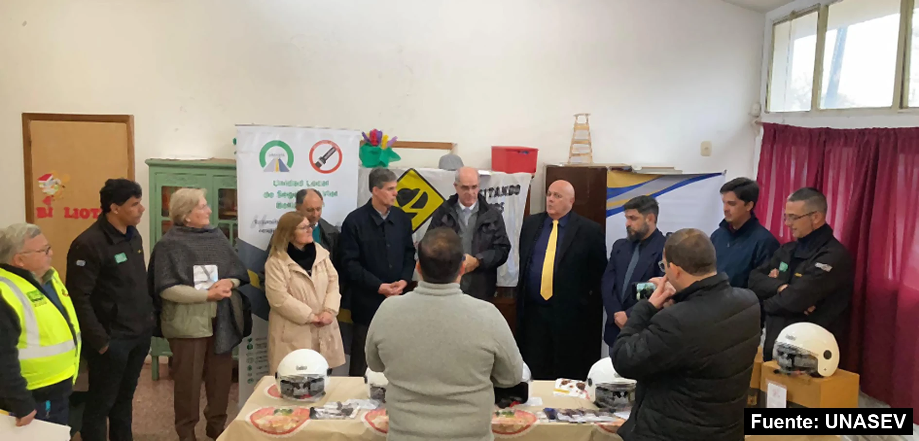 Autoridades e integrantes de la Unidad Local de Seguridad Vial de Bella Unión reunidos en un salón, junto a una mesa con cascos y folletos y el pendón de la unidad local