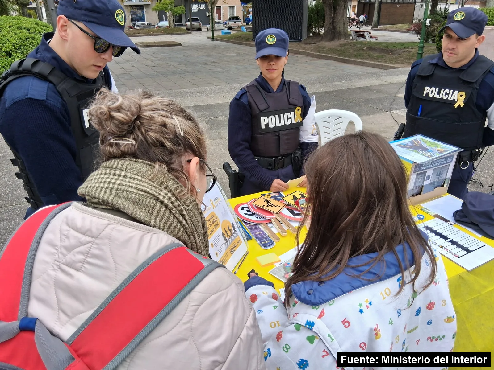 Mayo Amarillo en Melo 3 Policías comunitarios muestran señales de tránsito a una familia en un stand de Mayo Amarillo en Cerro Largo