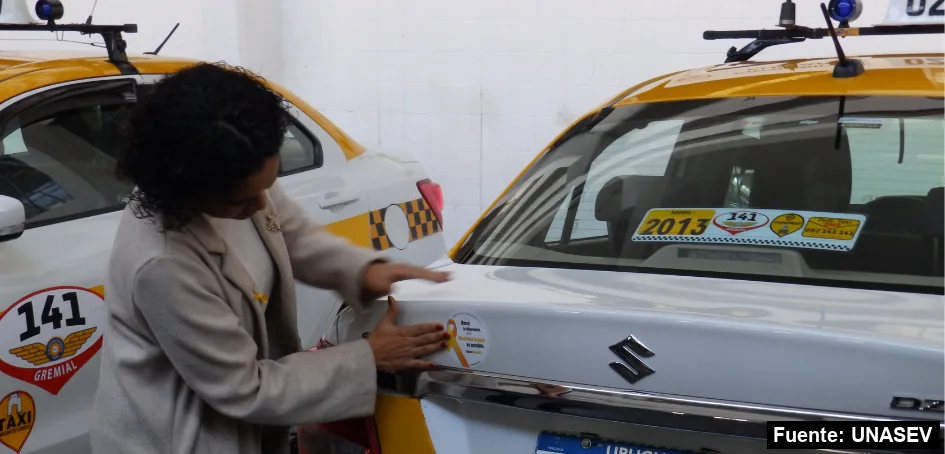 Una mujer pega el sticker de Mayo Amarillo en el baúl de un taxi de Montevideo.