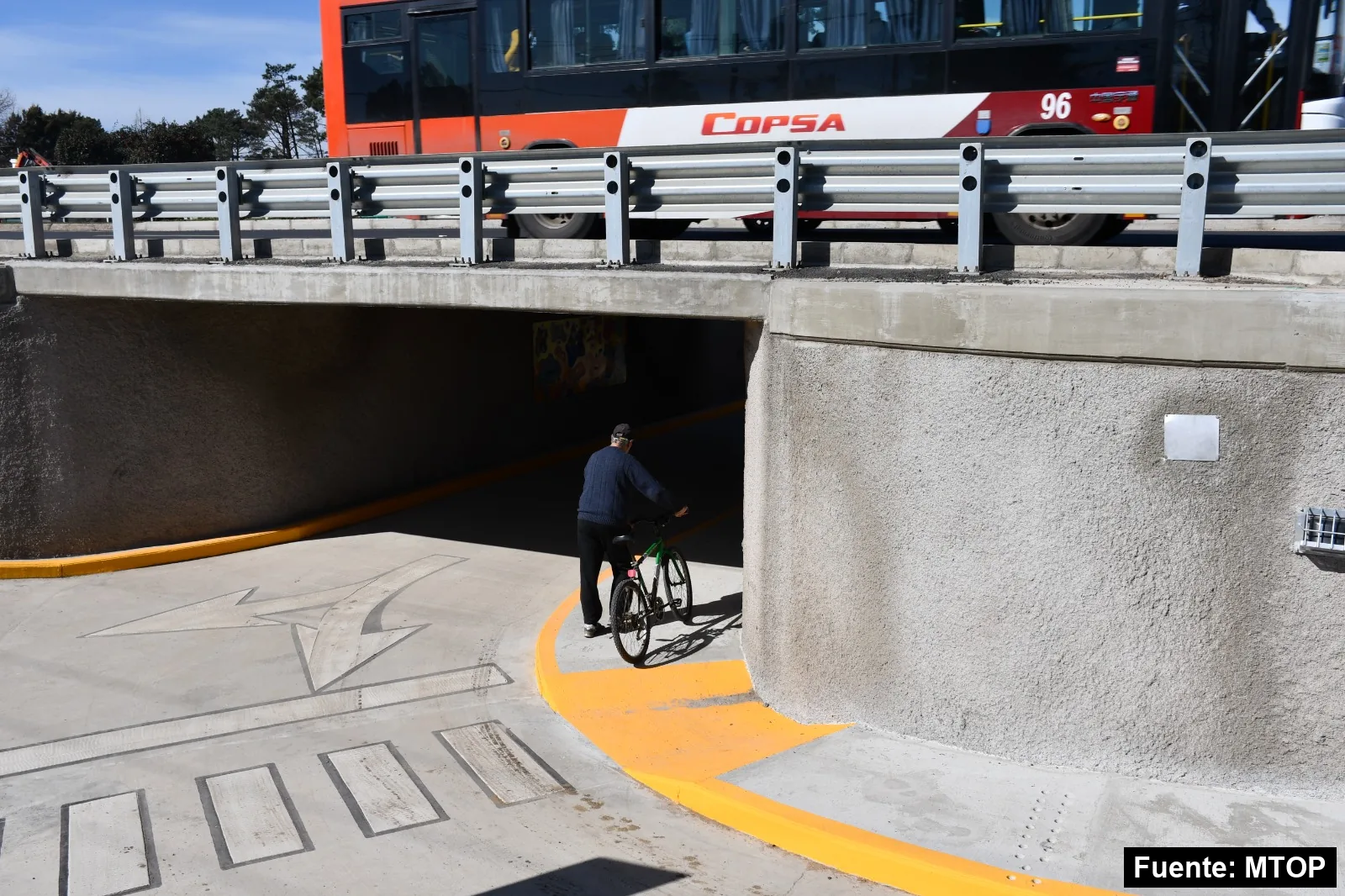 Una persona en bicicleta entra al túnel bajo la Ruta Interbalnearia en Pinamar mientras un ómnibus pasa por arriba