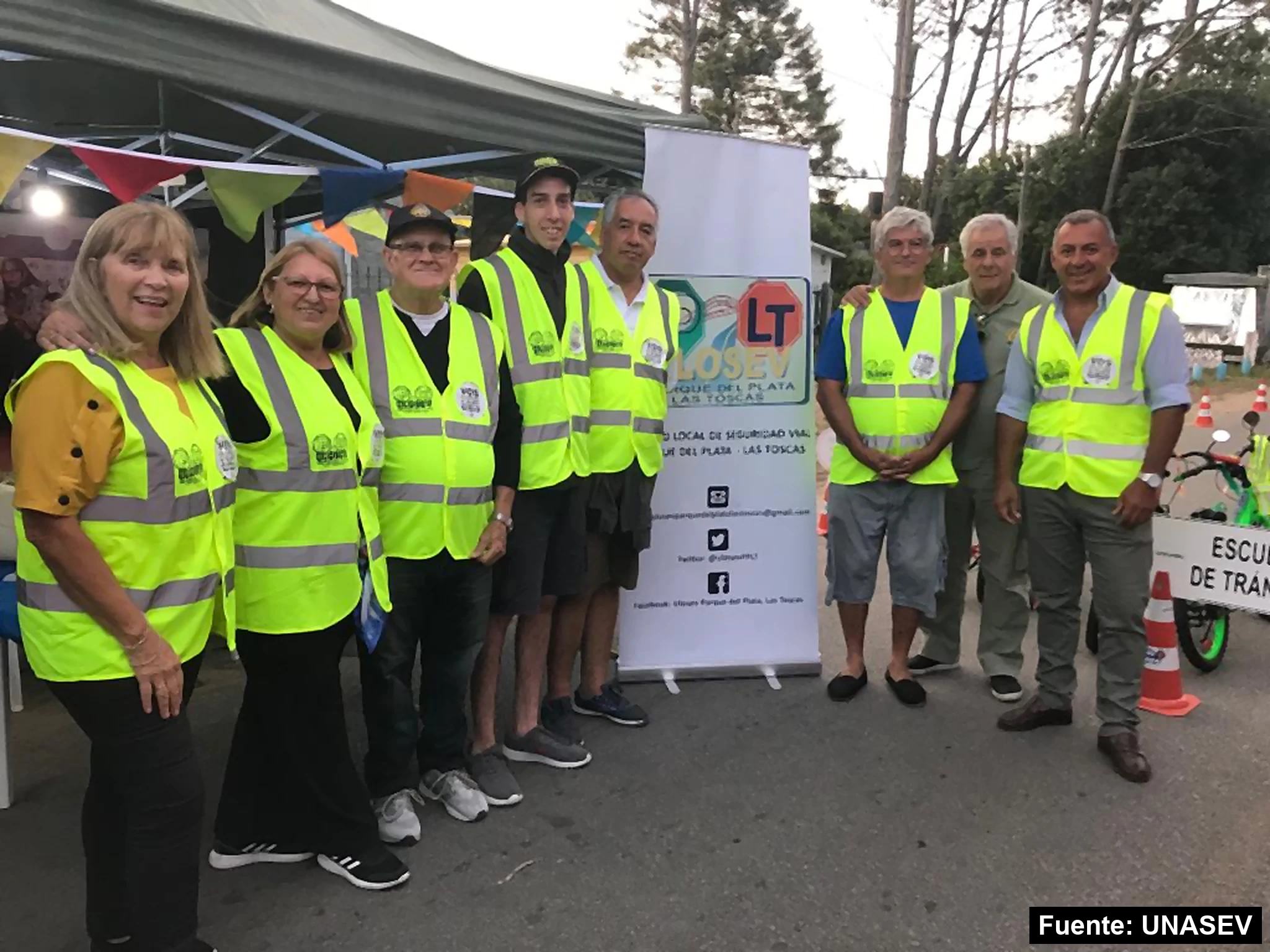 Integrantes de la ULOSEV de Parque del Plata y Las Toscas con chalecos reflectivos junto a su cartel en una feria de seguridad vial