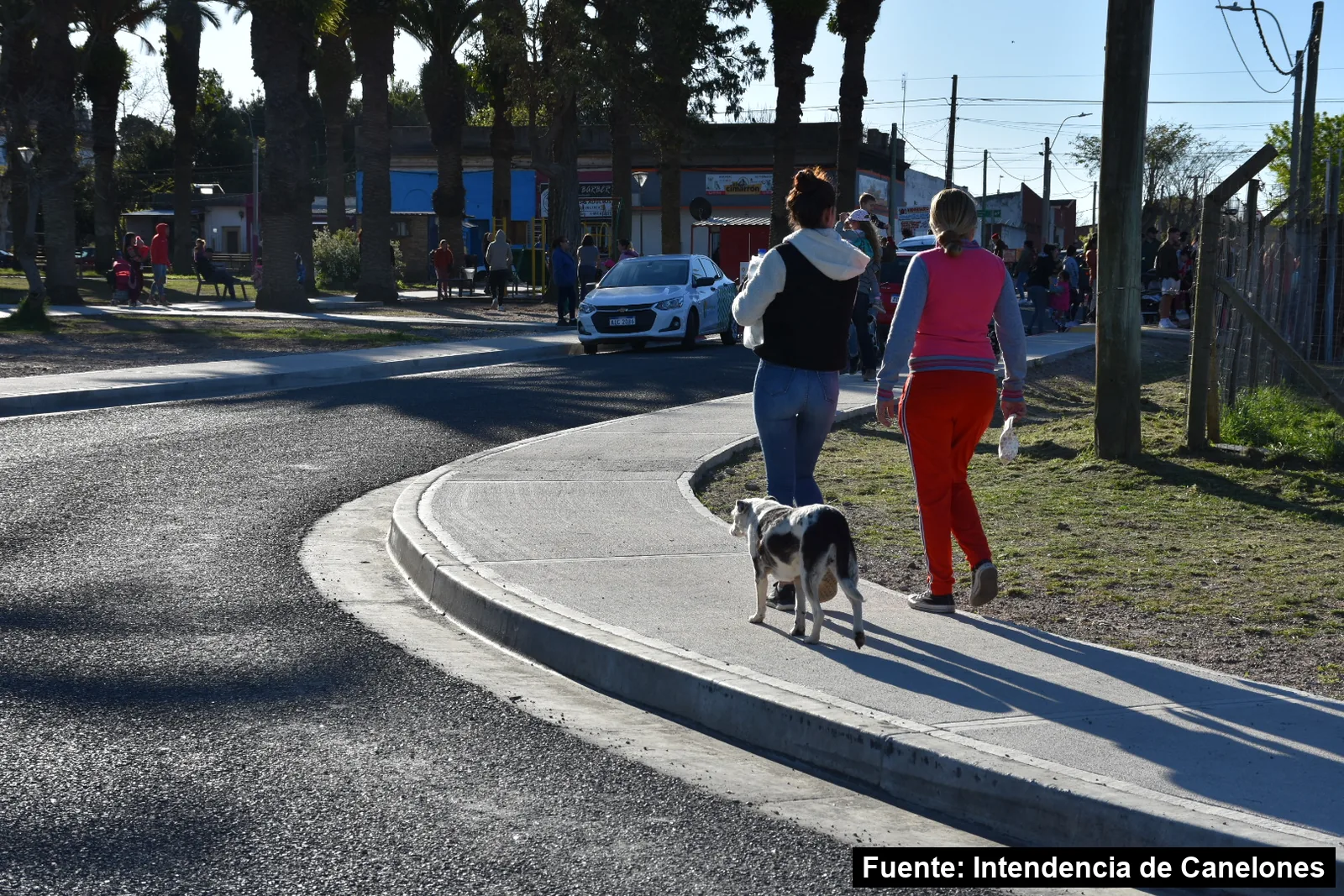 Mayo Amarillo en Joaquín Suárez 3 Dos personas caminan con un perro por una vereda nueva de hormigón en el centro de Joaquín Suárez